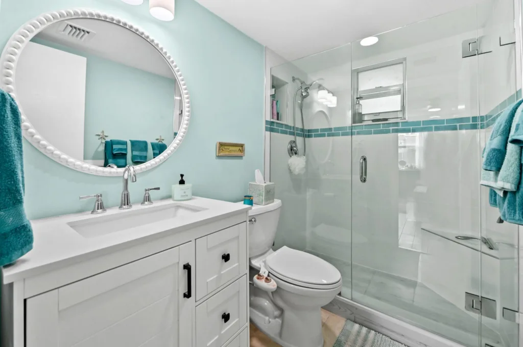 20260916183706333792000000-o - Lake Worth Homes - Lake Worth Homes Bright bathroom with turquoise walls, white vanity, oval beaded mirror, and glass shower enclosure with a teal-tile band.