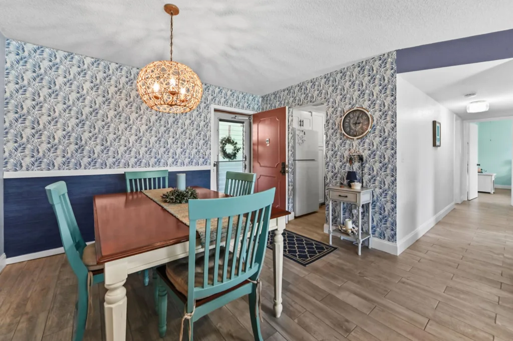 20260916183355291941000000-o - Lake Worth Homes - Lake Worth Homes Cozy dining room with turquoise chairs around a wooden table, palm-pattern wallpaper, and a wicker pendant light above the table.