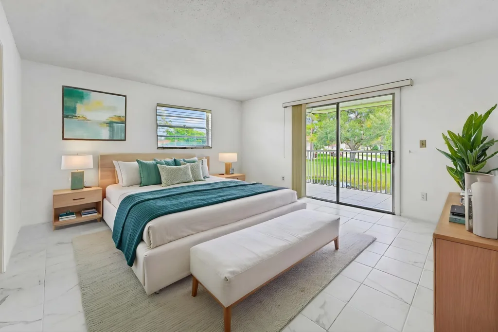 20260923173328876714000000-o - Lake Worth Homes - Lake Worth Homes Bright modern bedroom with a king bed, teal throw, and matching pillows facing a sliding glass door to a balcony outside.