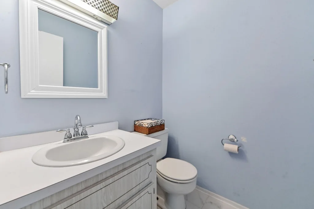 20260909143344267427000000-o - Lake Worth Homes - Lake Worth Homes Small bathroom with light blue walls, white vanity and sink, chrome faucet, and a rectangular mirror above the counter.