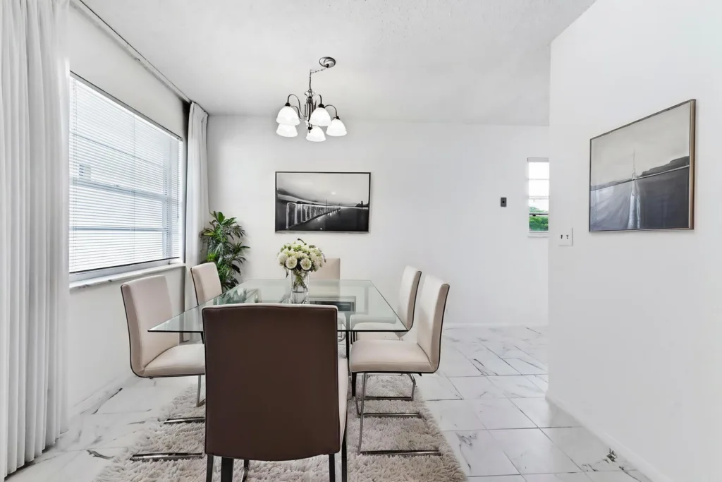 20260923153317315099000000-o - Lake Worth Homes - Lake Worth Homes Modern dining room with a glass table, beige chairs, and a chandelier in a bright white space.