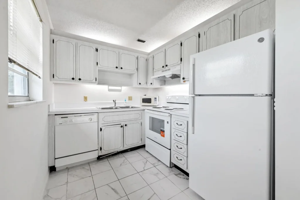 20260909143336127911000000-o 1 - Lake Worth Homes - Lake Worth Homes Bright white kitchen with upper and lower cabinets, a sink, and full set of white appliances (refrigerator, stove, microwave, dishwasher).