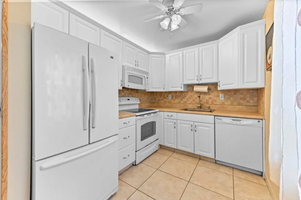 20260917212336985248000000-o - Lake Worth Homes - Lake Worth Homes Bright white kitchen with a full-size fridge, microwave, stove, dishwasher, and beige tiled backsplash.