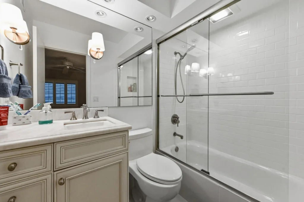 20260923233629355097000000-o - Lake Worth Homes - Lake Worth Homes Cream bathroom vanity with a marble countertop, double sinks, and chrome fixtures next to a toilet and a glass-enclosed shower.