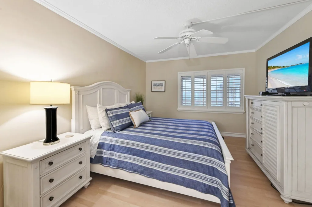 20260923233600505305000000-o - Lake Worth Homes - Lake Worth Homes Coastal-style bedroom with a white wooden bed, blue striped quilt, matching pillows, and white nightstands under a ceiling fan.