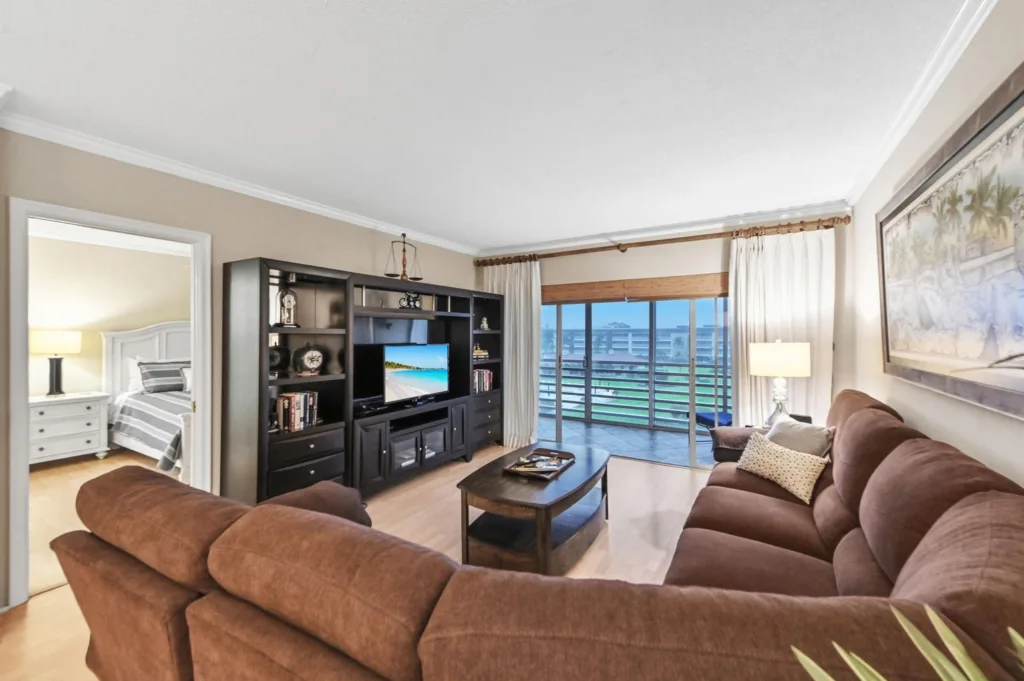 20260923233137493602000000-o - Lake Worth Homes - Lake Worth Homes Living room with a large brown sectional sofa, a dark wood entertainment center with TV, and a coffee table, opening to a sliding glass door balcony view.