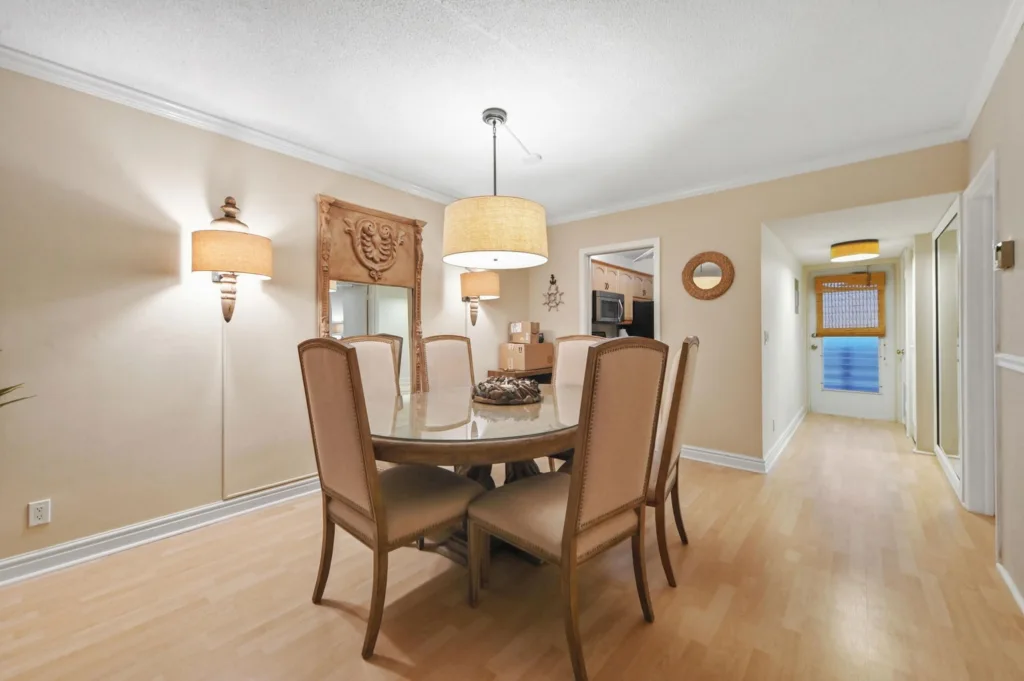 20260923233049150873000000-o - Lake Worth Homes - Lake Worth Homes Dining room with glass-top table and six beige upholstered chairs, warm pendant light, and wood floor.