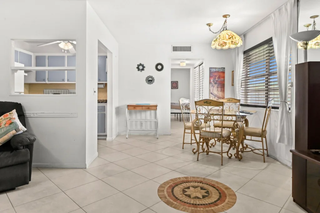 20260921183300142800000000-o - Lake Worth Homes - Lake Worth Homes Bright open living-dining area with a glass dining table and ornate cream chairs, large window with blinds, and tiled floor sheens.