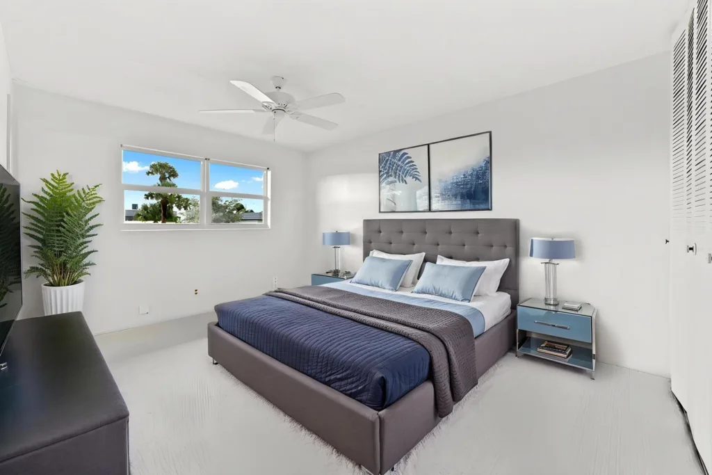 20260924144133774975000000-o - Lake Worth Homes - Lake Worth Homes Modern gray upholstered bed with blue bedding and matching nightstands in a bright white bedroom.