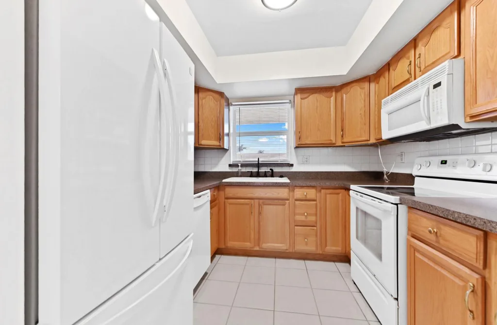 20260924144016862632000000-o - Lake Worth Homes - Lake Worth Homes U-shaped kitchen with oak cabinets, white appliances, and a window above the sink.