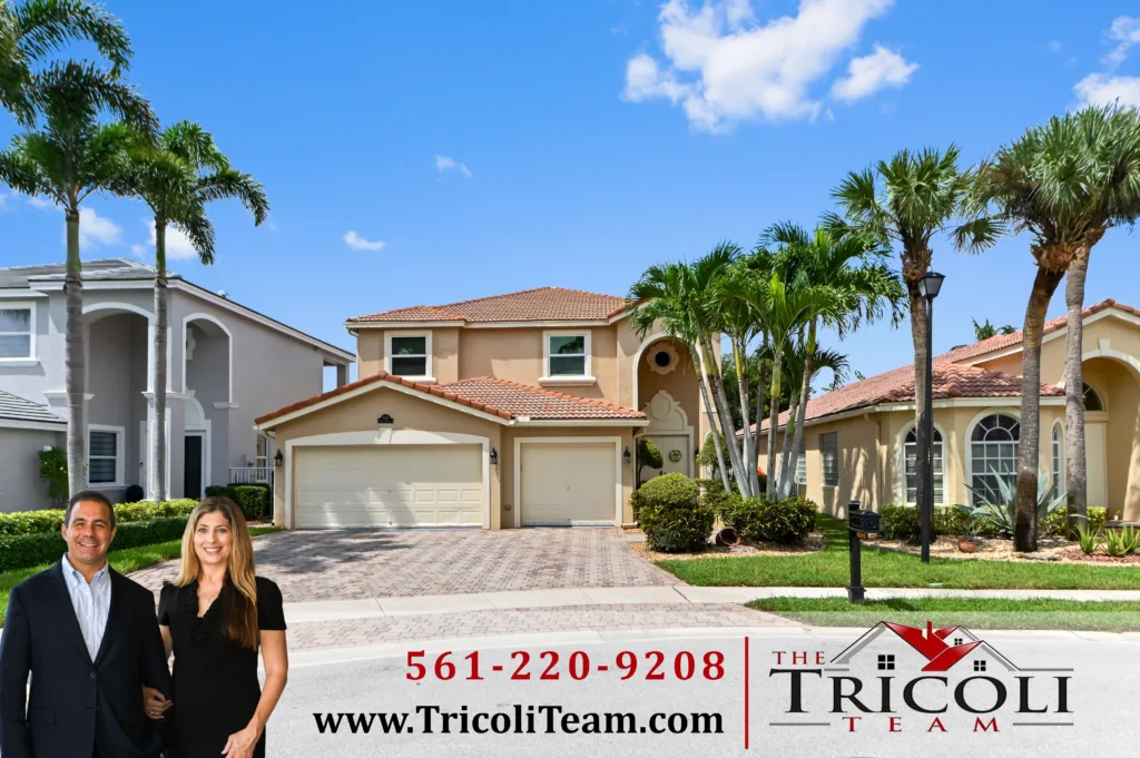 Homes for Sale in Villages of Windsor Lake Worth FL 33467 1 - Lake Worth Homes - Lake Worth Homes Two real estate agents stand smiling in front of a row of palm-lined homes on a sunny day, with a'Tricoli Team' sign visible.