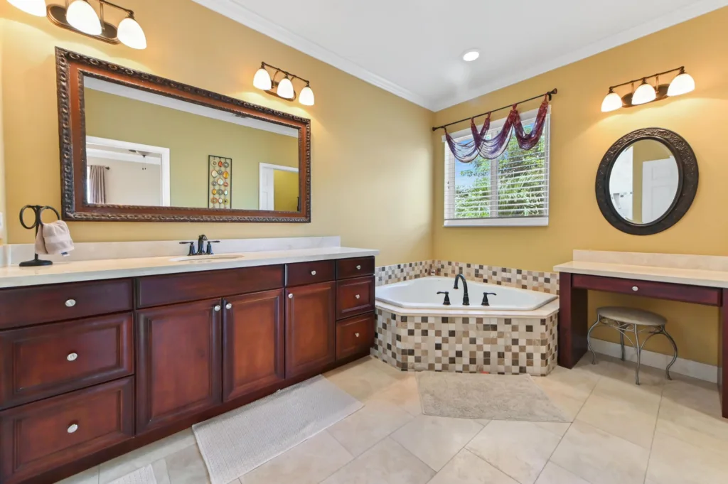 20260922220548107328000000-o - Lake Worth Homes - Lake Worth Homes Spa-style bathroom with a dark wood double vanity, large ornate framed mirror, and a mosaic-tile corner tub.
