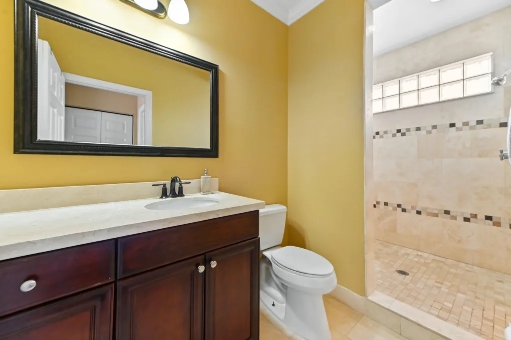 20260922220538863514000000-o - Lake Worth Homes - Lake Worth Homes Bathroom with yellow walls, dark wood vanity, white countertop and sink, and a large black-framed mirror above it.