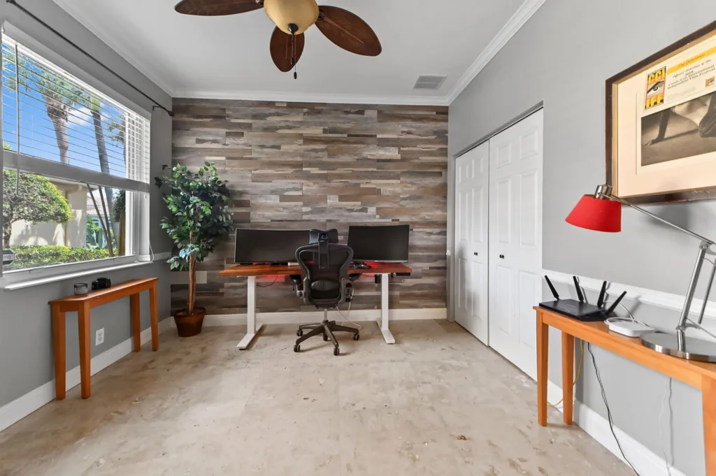 20260922220307156084000000-o - Lake Worth Homes - Lake Worth Homes Home office with a dual-monitor computer setup on a wooden desk against a gray-toned stone accent wall, and an ergonomic chair in front.