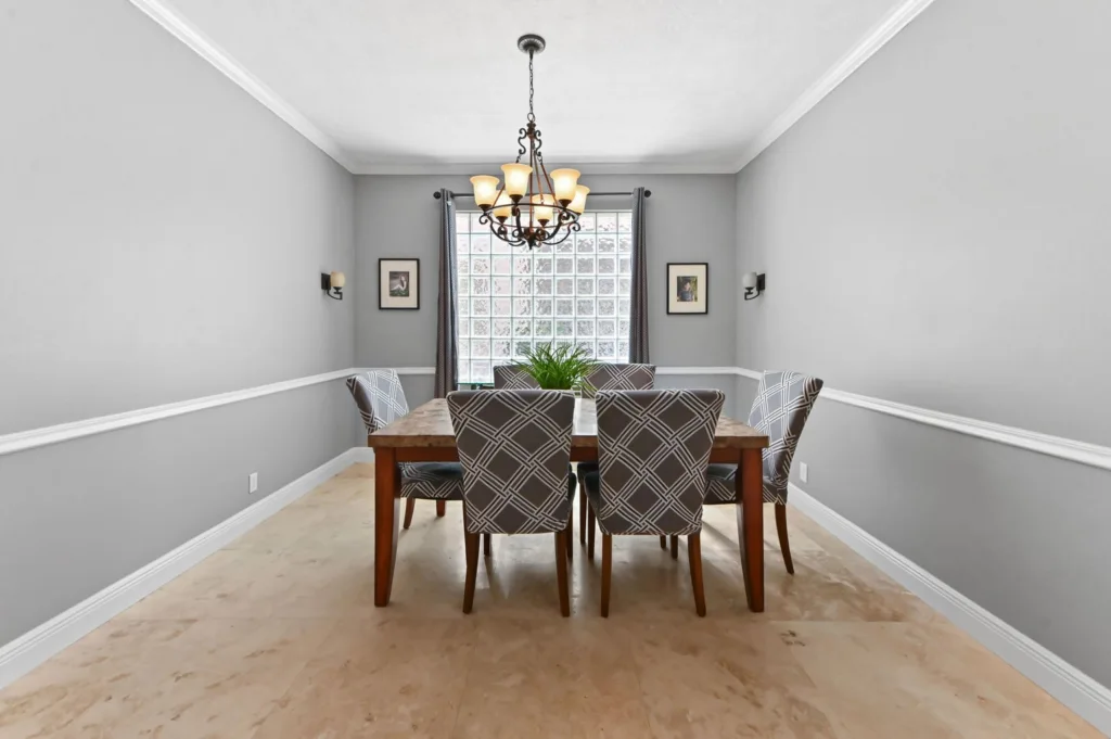 20260922220247671510000000-o - Lake Worth Homes - Lake Worth Homes Dining room with a wooden six-seat table, six patterned chairs, a wrought-iron chandelier, gray walls, and a glass-block window with sheer curtains.