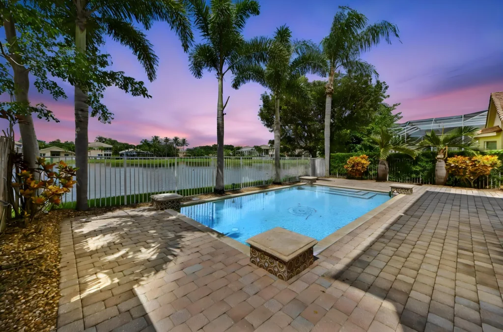 20260922221833643754000000-o - Lake Worth Homes - Lake Worth Homes Poolside with palm trees, overlooking a lake at sunset; blue water and pink-purple sky.