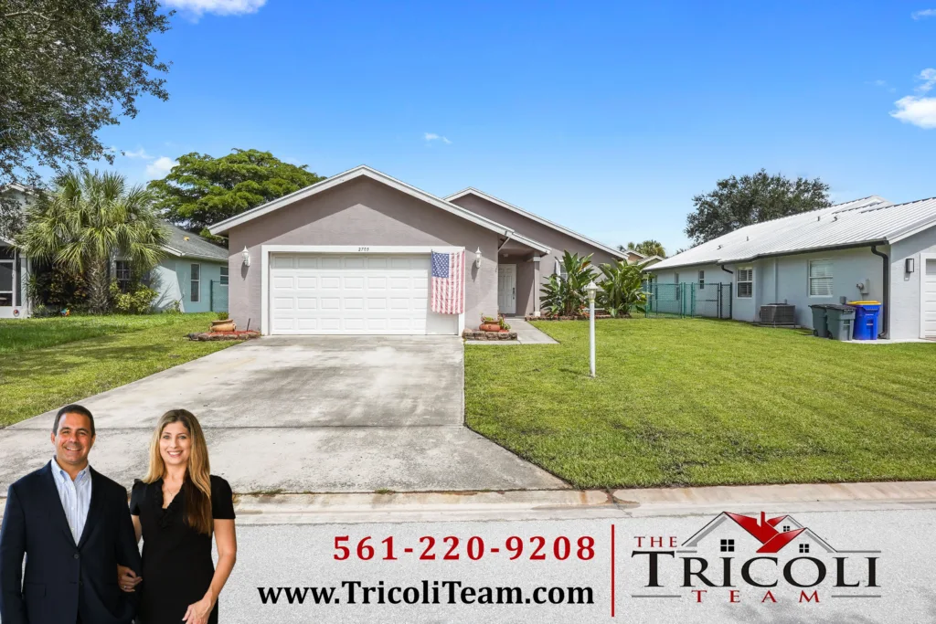 Homes for Sale in River Forest Stuart FL 34997 - Lake Worth Homes - Lake Worth Homes Front view of a single-story house with an American flag on the garage, and two real estate agents standing in the driveway (Tricoli Team ad).