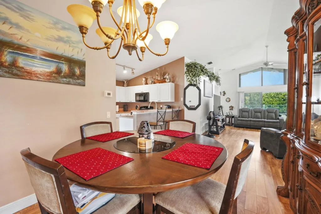 20260924161810542957000000-o - Lake Worth Homes - Lake Worth Homes Round dining table with red placemats in an open-plan kitchen and living room, with a brass chandelier overhead.