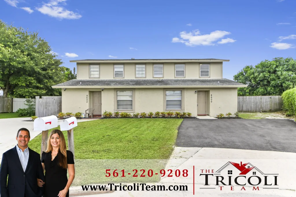 Homes for Sale in Parkway Village West Palm Beach FL 33403 2 - Lake Worth Homes - Lake Worth Homes Two real estate agents in business attire stand in front of a beige duplex with a manicured lawn, advertising The Tricoli Team (phone 561-220-9208).
