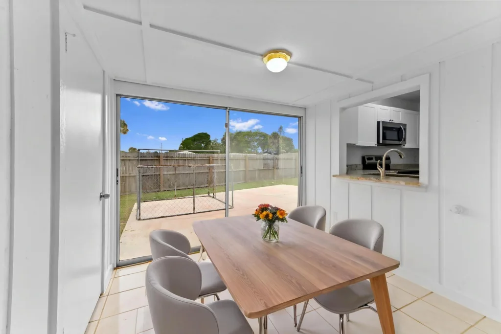 20260930184606230421000000-o - Lake Worth Homes - Lake Worth Homes Bright dining area with a wooden table and six gray chairs, sliding glass door opening to a fenced backyard beyond the patio.