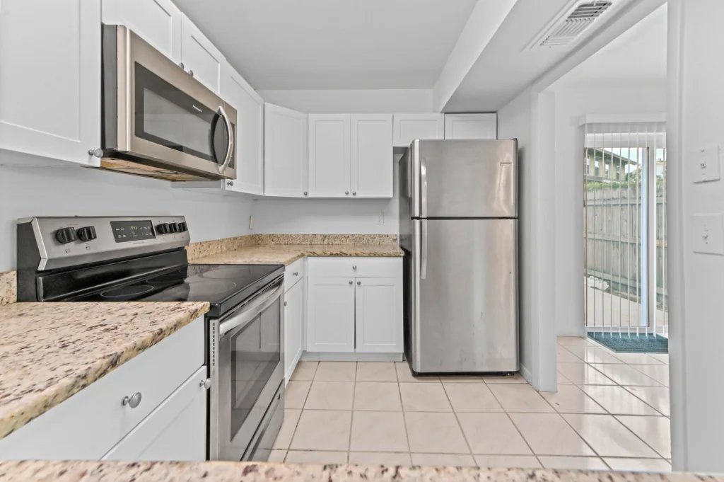 20260930184547633626000000-o - Lake Worth Homes - Lake Worth Homes Bright white kitchen with granite countertops and stainless steel appliances (microwave, stove, and refrigerator).