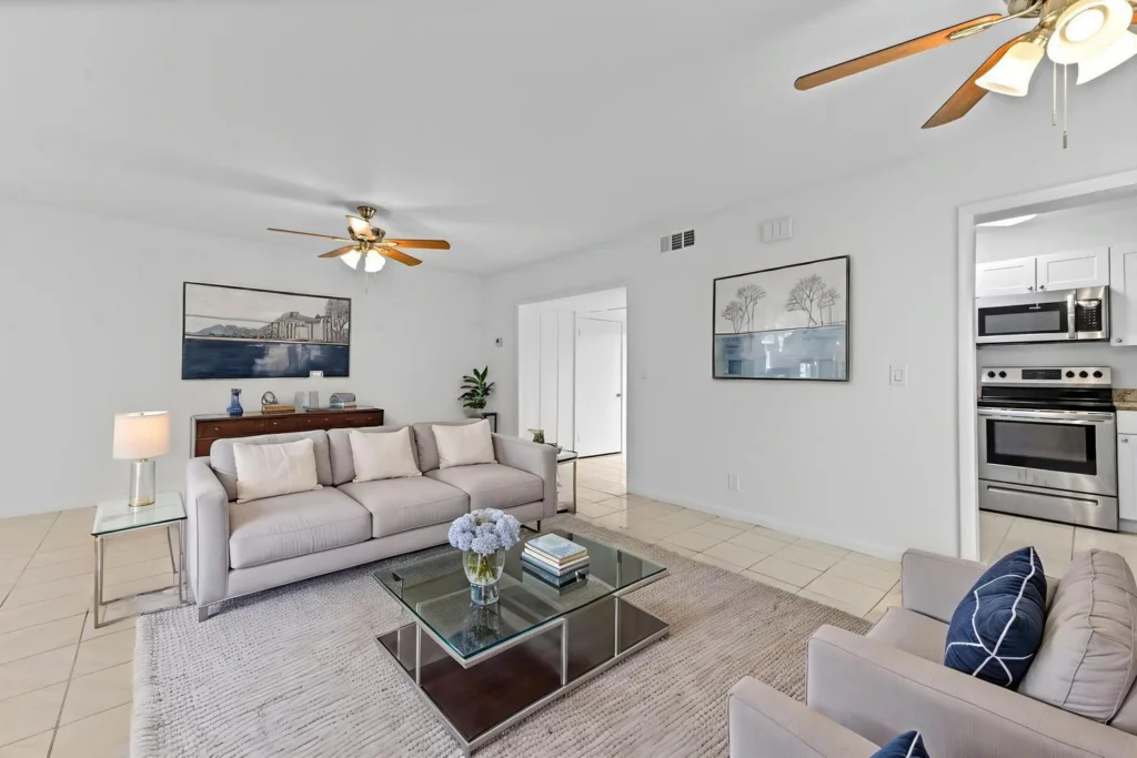 20260930184431778178000000-o - Lake Worth Homes - Lake Worth Homes Open living room with light gray sofa, glass coffee table, and neutral rug; kitchen visible to the right.