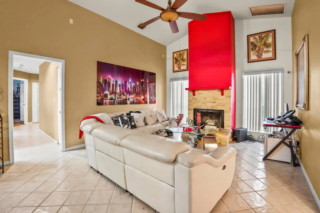 20261001130156059160000000-o - Lake Worth Homes - Lake Worth Homes Spacious living room with a white sectional sofa facing a tall red fireplace and stacked stone surround.