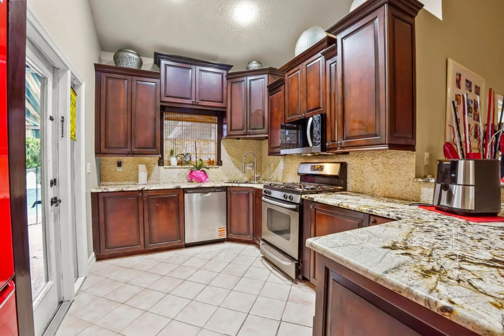 20261001130056359467000000-o - Lake Worth Homes - Lake Worth Homes Rustic-style kitchen with dark wood cabinets, granite countertops, and stainless steel appliances (stove, microwave, dishwasher) across L-shaped counters.