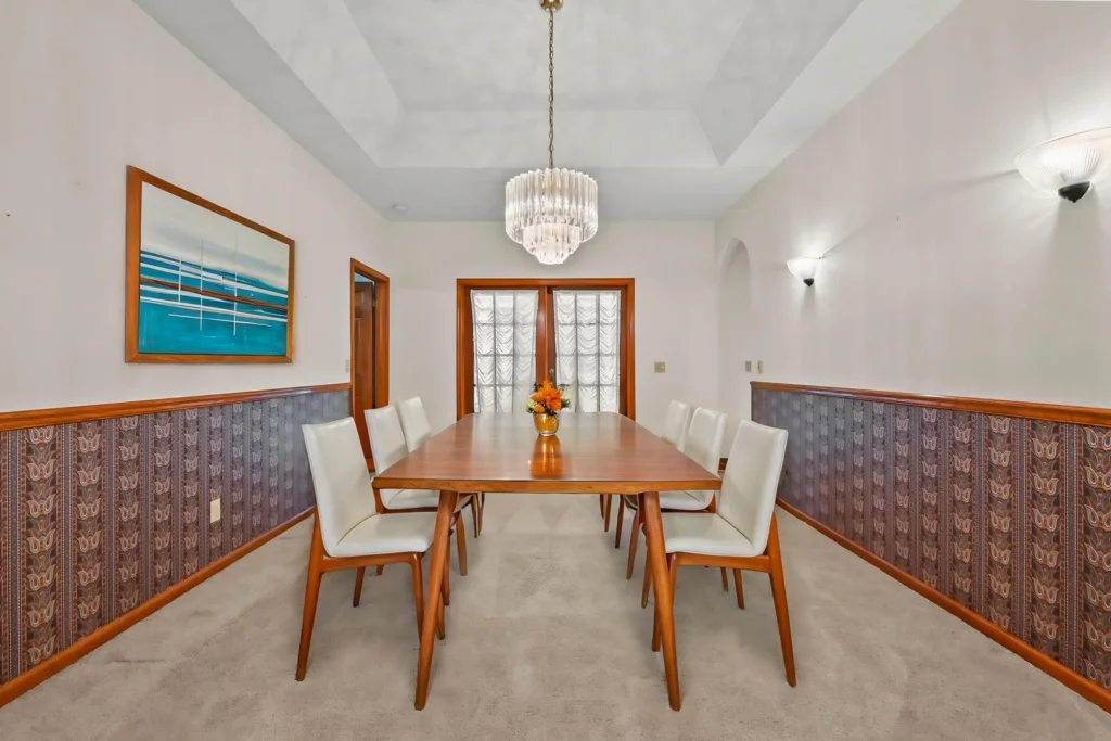 20260930222656610010000000-o - Lake Worth Homes - Lake Worth Homes A mid-century dining room with a long wooden table, white upholstered chairs, and a crystal chandelier overhead.