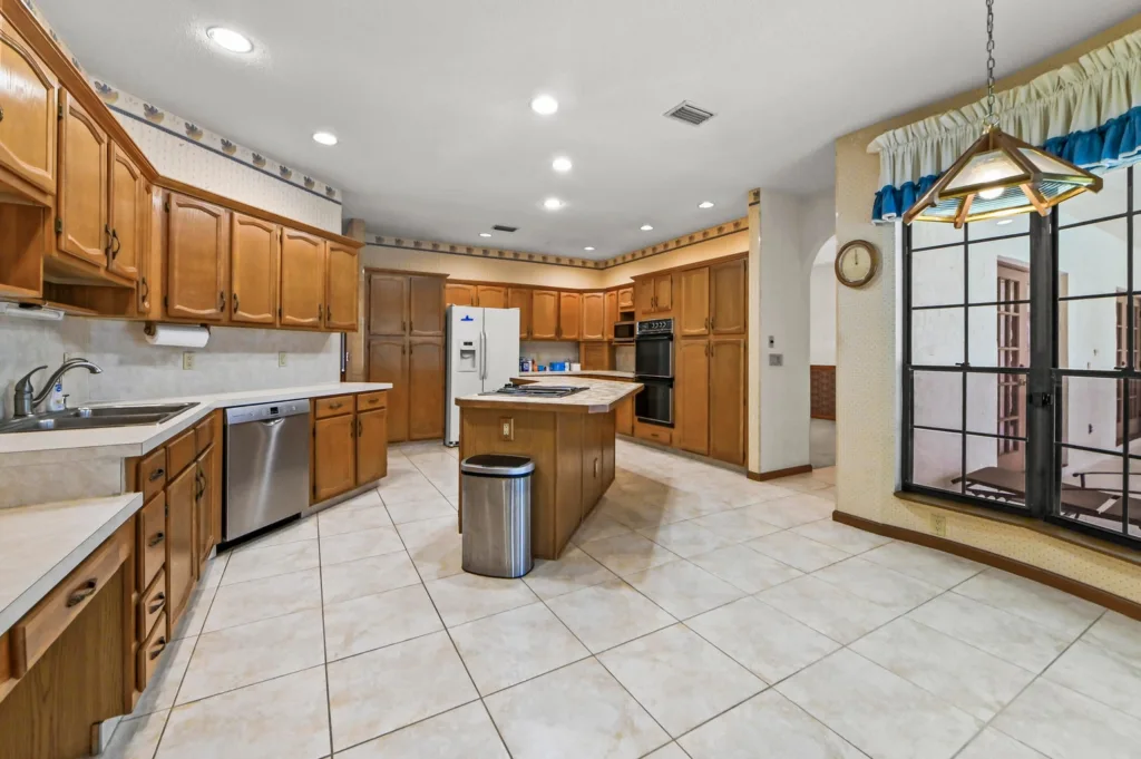 20260930221138065811000000-o - Lake Worth Homes - Lake Worth Homes Spacious kitchen with oak cabinets, a central island, stainless fridge and dishwasher, and tiled floor.