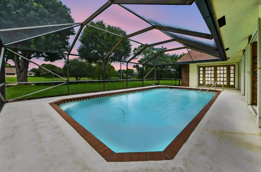 20260930223005538467000000-o 1 - Lake Worth Homes - Lake Worth Homes Enclosed backyard pool with turquoise water, brick-edged liner, and a concrete deck beside a house with glass doors at sunset.