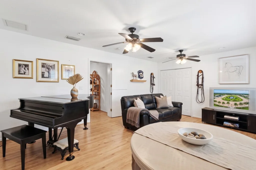 20260925163810381576000000-o - Lake Worth Homes - Lake Worth Homes Bright living room with a black grand piano on the left, a leather sofa, round coffee table, and a TV on the right wall.