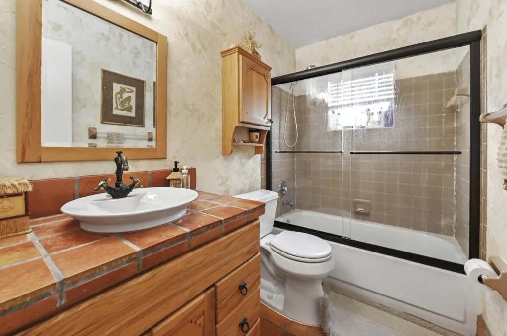 20260925125530076510000000-o - Lake Worth Homes - Lake Worth Homes Rustic bathroom with a brick-style tiled vanity, white vessel sink, black faucet, and large glass-paneled shower.