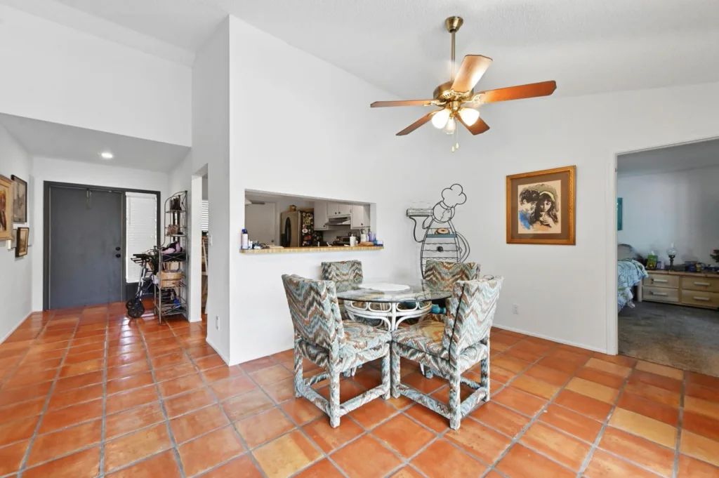 20260925125300910199000000-o - Lake Worth Homes - Lake Worth Homes Dining area with round glass table and patterned chairs on terracotta tile floor; open kitchen to the left and a wall with a chef drawing to the right.