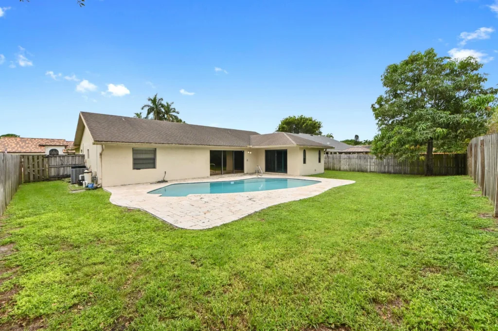 20260925125938978316000000-o - Lake Worth Homes - Lake Worth Homes Backyard with an in-ground pool, beige house, and wooden fence under a bright blue sky.
