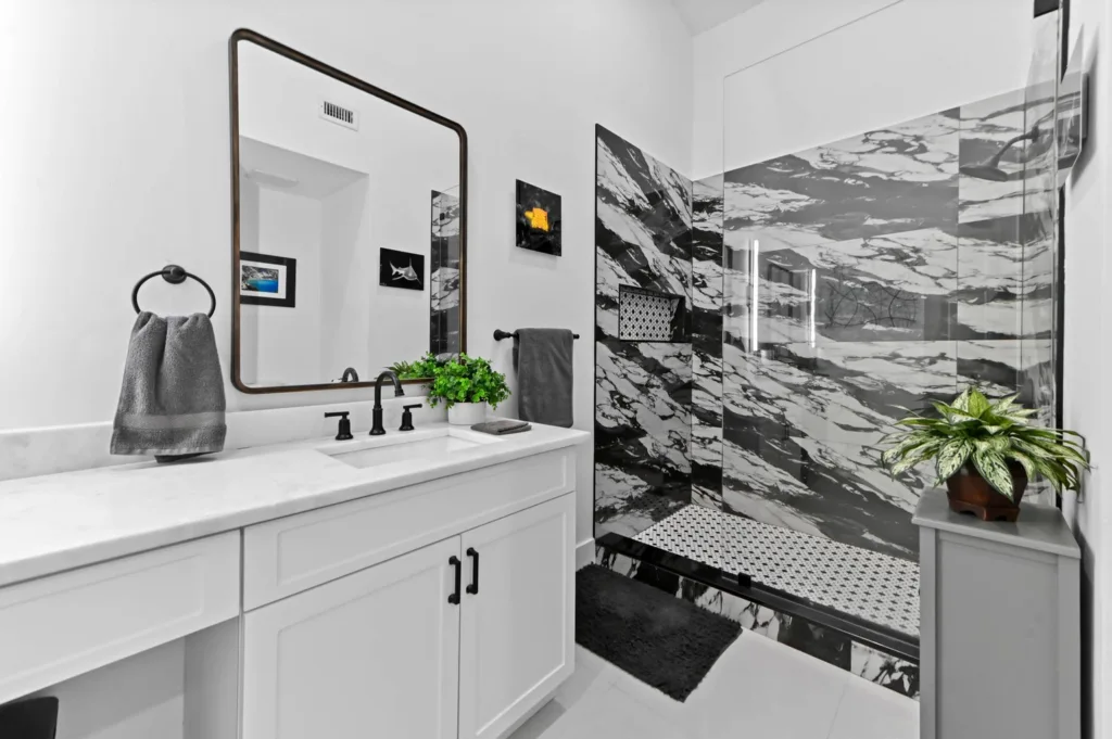 Modern white bathroom featuring a marble shower, black faucet and hardware, and a white vanity with a mirror.