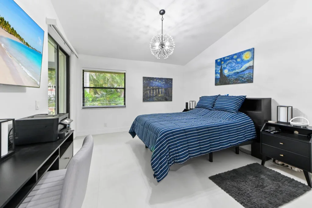 Bright modern bedroom with a queen bed in navy-blue striped bedding, black nightstands, and a starburst chandelier.