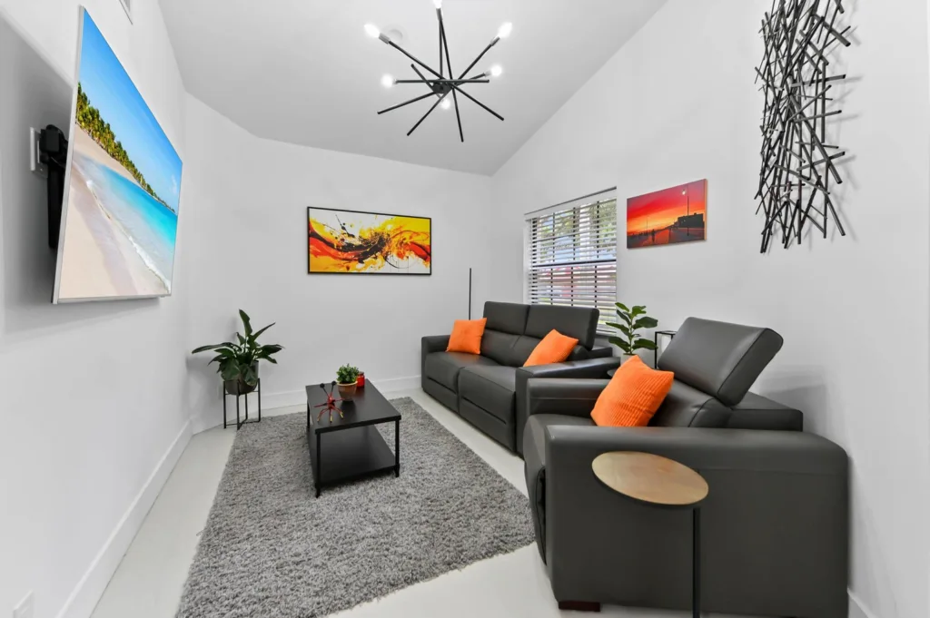 Modern living room with two gray leather sofas, orange pillows, a black coffee table, and a gray shag rug.