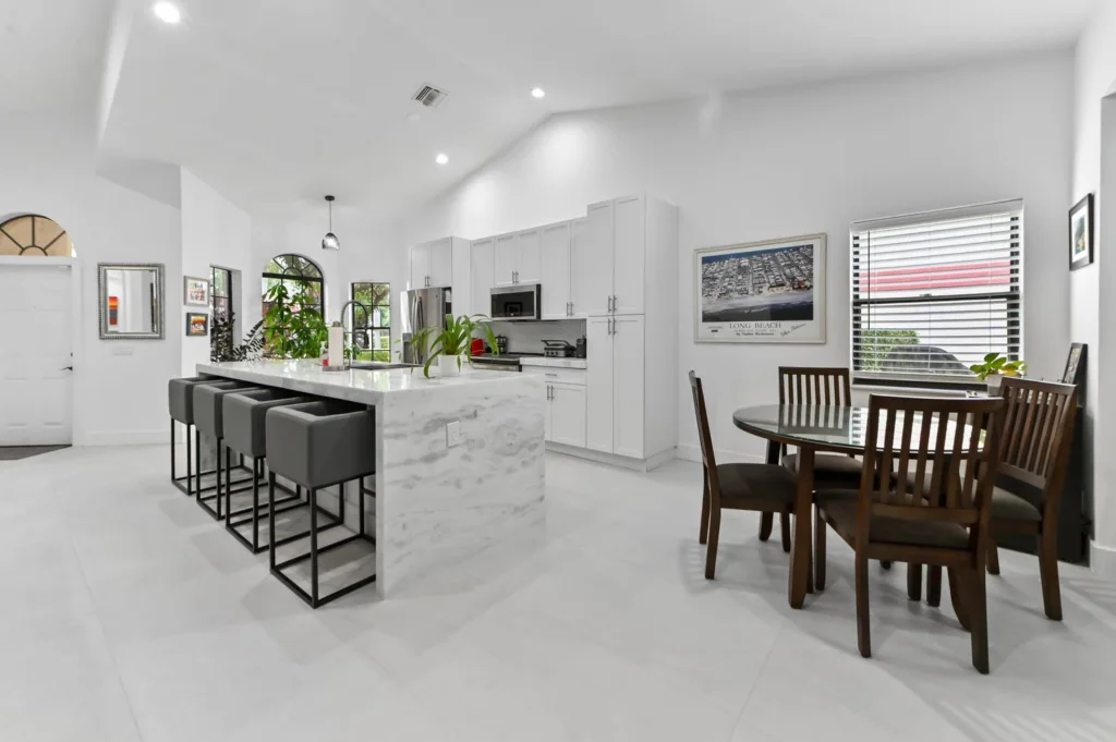 Bright open-plan kitchen with a marble island and five gray bar stools.