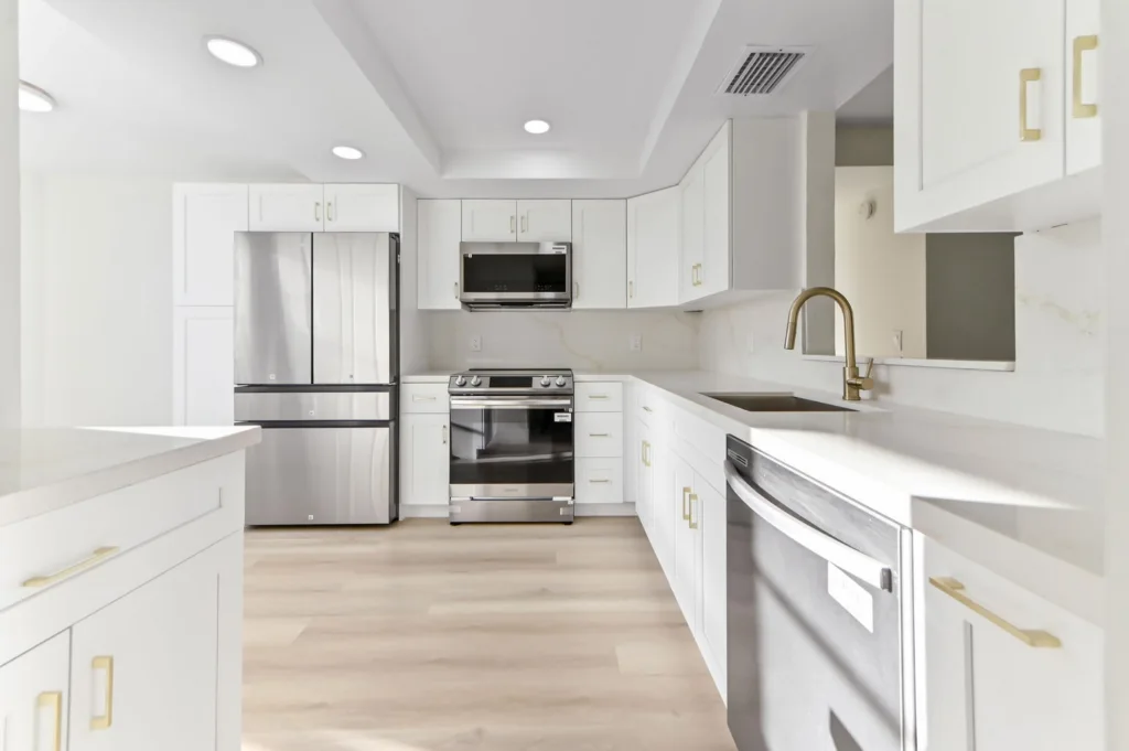 20260929180409992375000000-o - Lake Worth Homes - Lake Worth Homes Bright white kitchen with stainless steel refrigerator, oven, microwave, and dishwasher, set on light wood flooring.