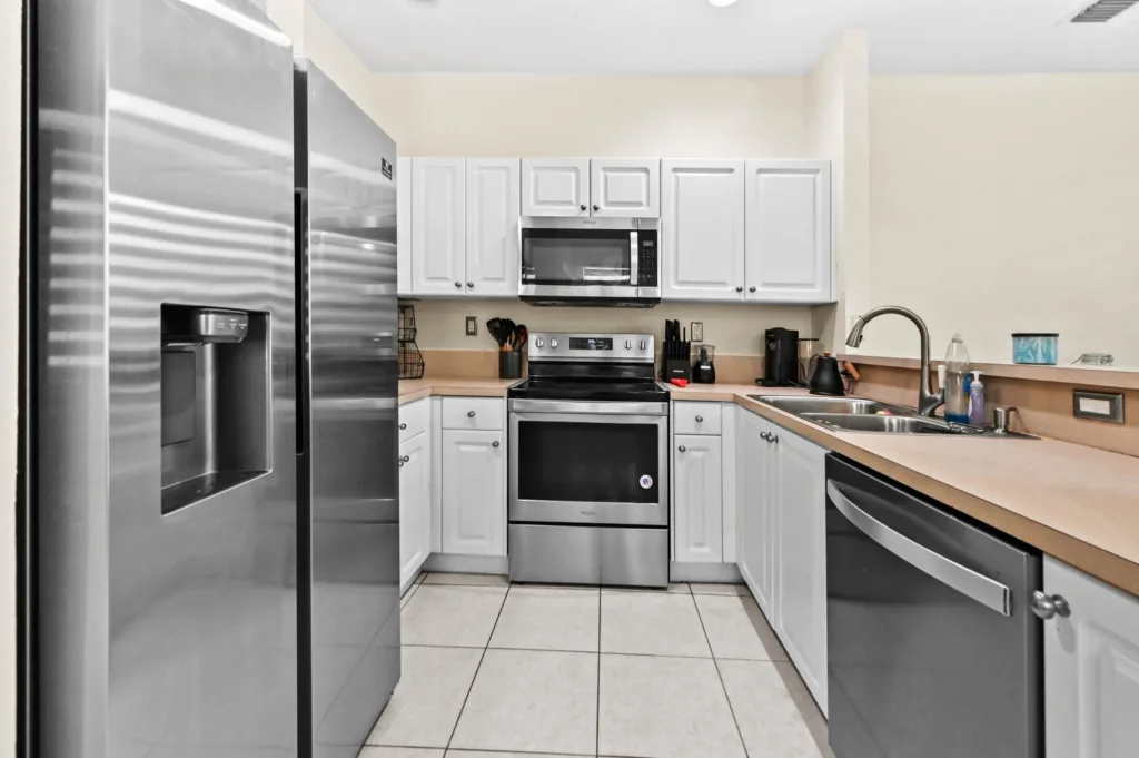 Kitchen with stainless steel appliances: large refrigerator left, stove with microwave above, white cabinets, and a double sink along the right countertop.