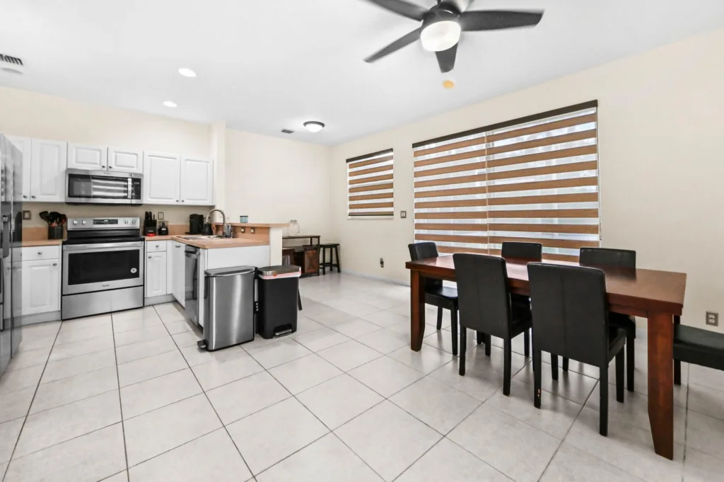 Open-concept kitchen with white cabinets, stainless steel appliances, and a wooden dining table with six black chairs.