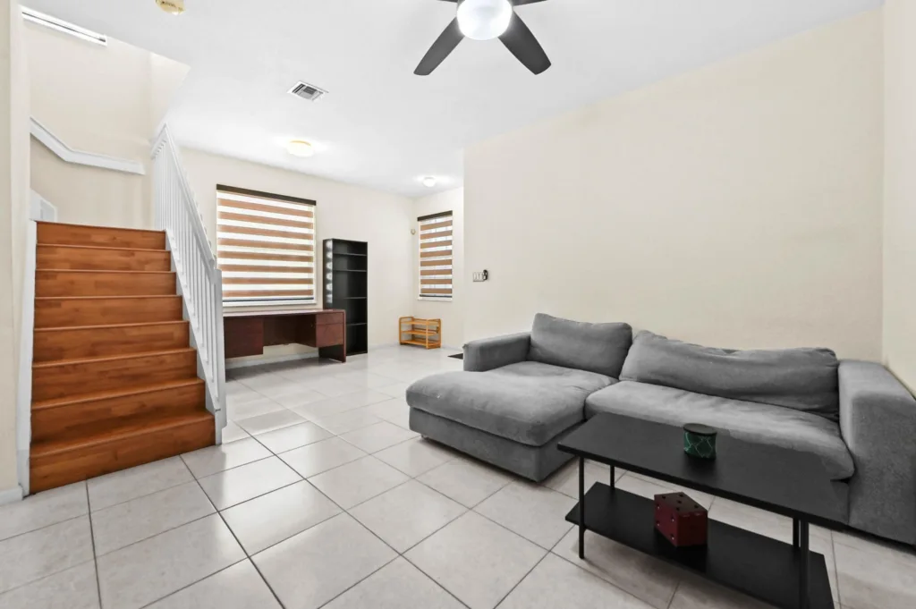 Bright living room with a gray L-shaped sofa, black coffee table, and wooden stairs on the left side.