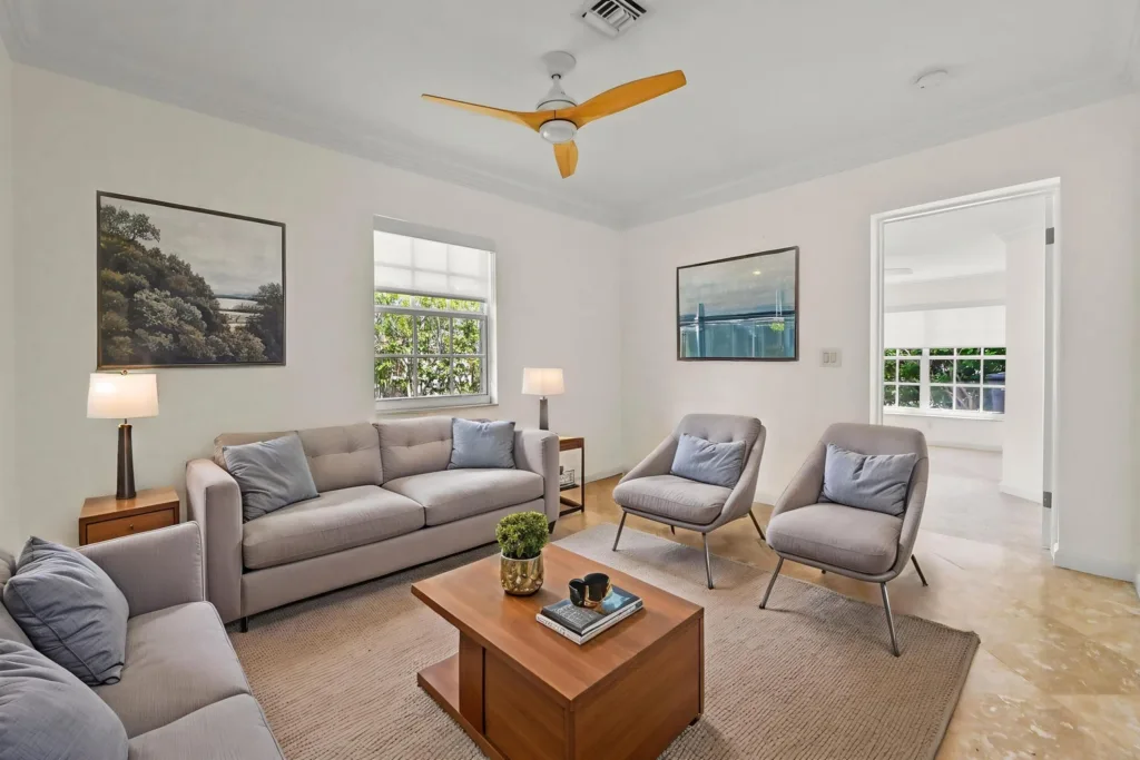 Modern living room with light gray sofa and two matching chairs around a wooden coffee table; neutral decor and framed art on light walls.