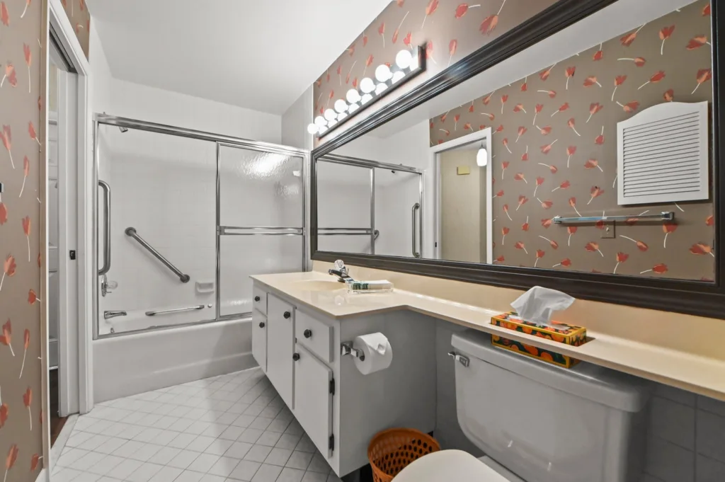 20261002200151760784000000-o - Lake Worth Homes - Lake Worth Homes Bathroom with floral wallpaper, large framed mirror, beige countertop, and a single-sink vanity adjacent to a toilet and tissue box.