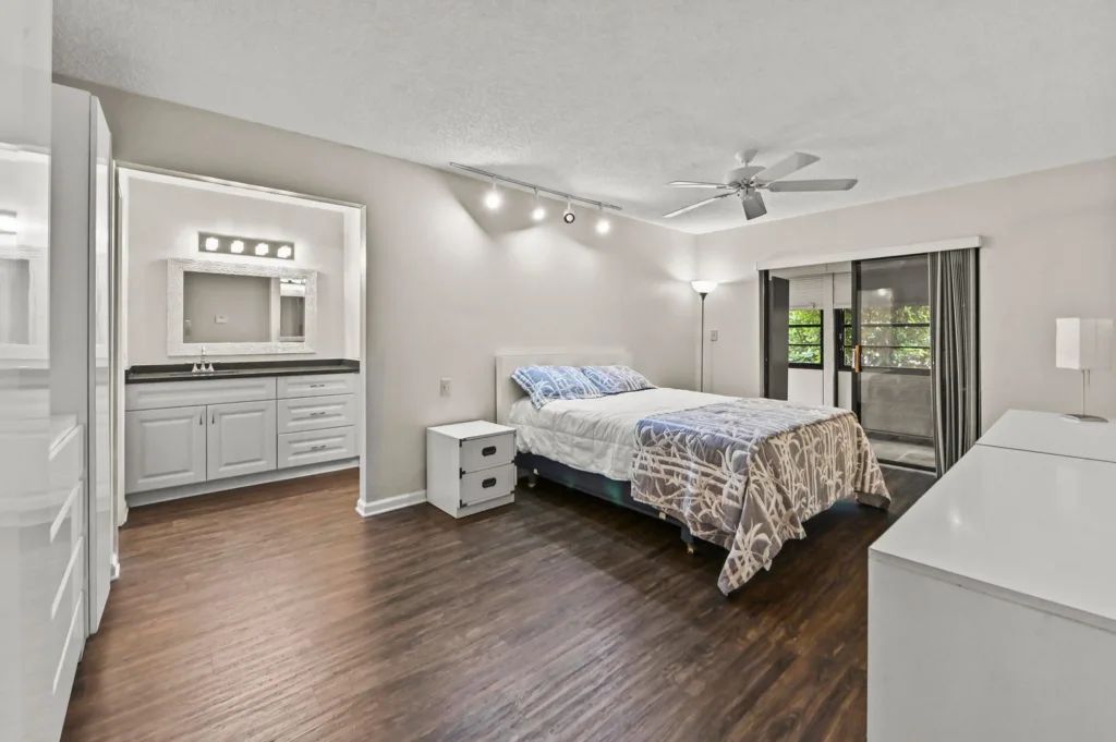 20261002200213588554000000-o - Lake Worth Homes - Lake Worth Homes Bright modern bedroom with a white bed, nightstands, dresser, and sliding glass door to a balcony/Patio area.