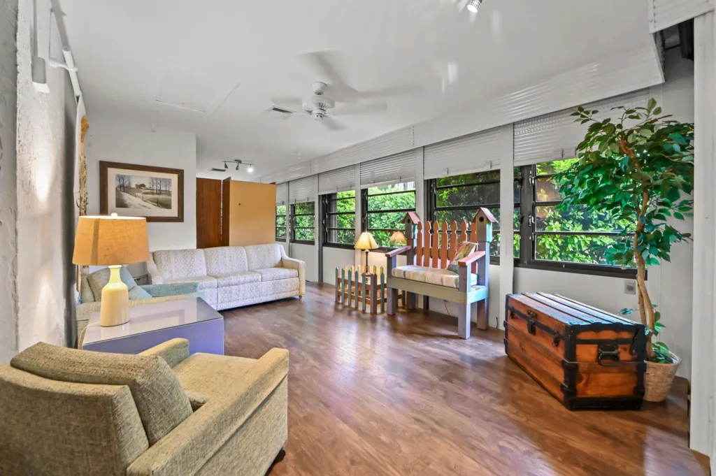 20261002200042975383000000-o - Lake Worth Homes - Lake Worth Homes Spacious living room with a pale sofa, gray chair, and large windows overlooking greenery outside.