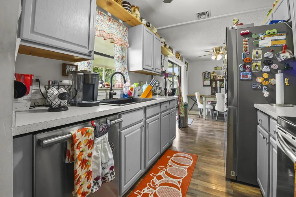 20261008152510493649000000-o - Lake Worth Homes - Lake Worth Homes Bright kitchen with gray cabinets, stainless fridge covered in magnets, and an orange rug on wood floor.