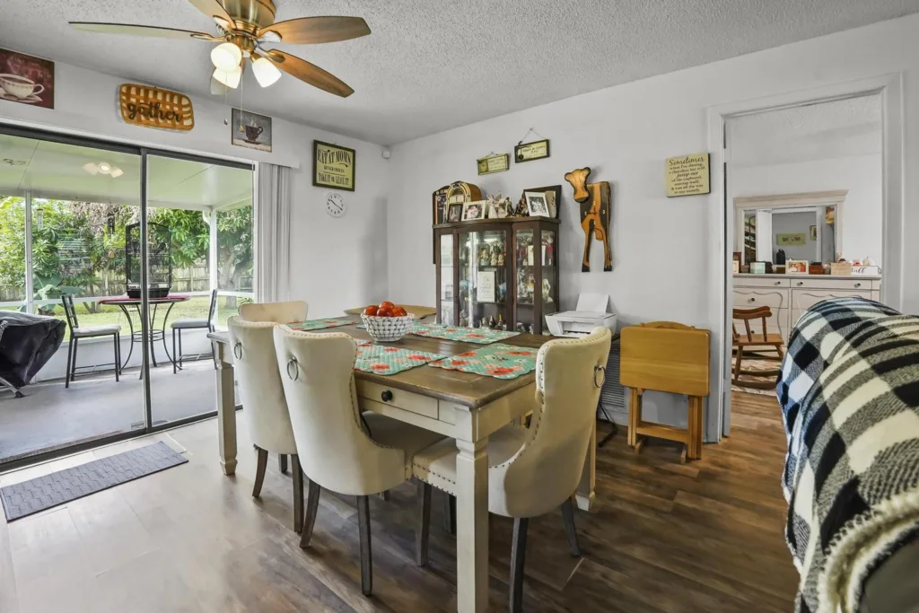 20261008152412506126000000-o - Lake Worth Homes - Lake Worth Homes Cozy dining room with a wooden table, cream upholstered chairs, and a glass patio door to a green backyard.