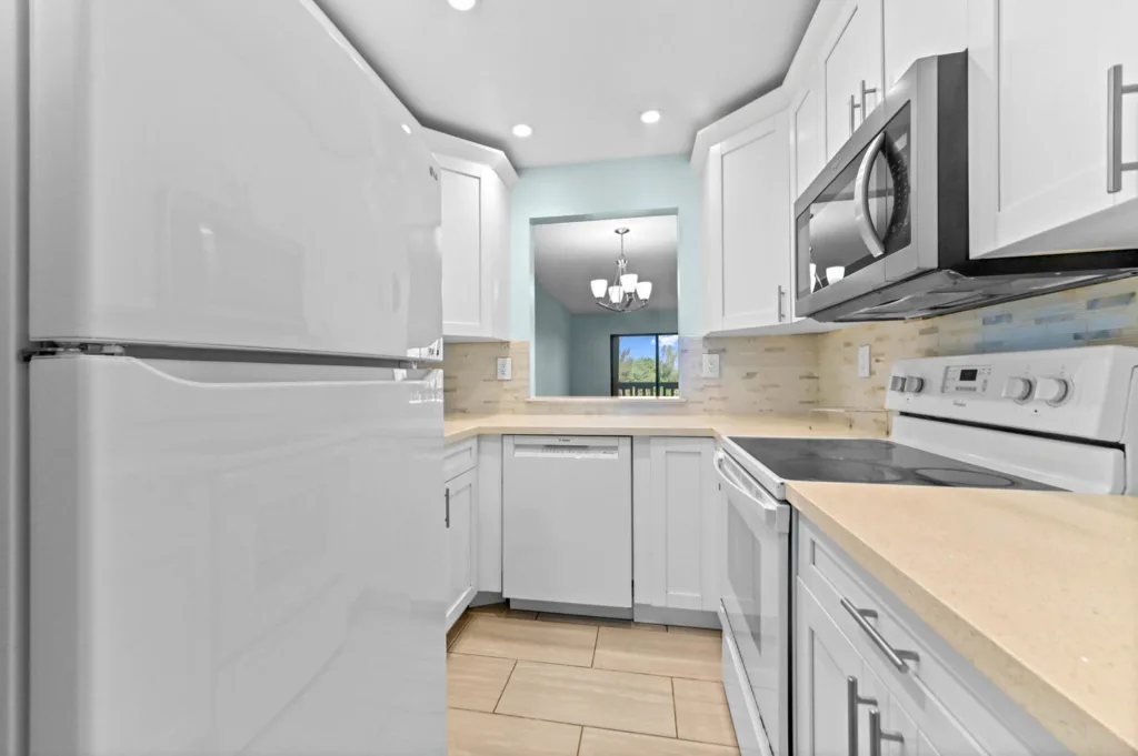 20261007172127093274000000-o - Lake Worth Homes - Lake Worth Homes Bright white kitchen with beige countertops, stainless appliances, and a pass-through to the dining room.